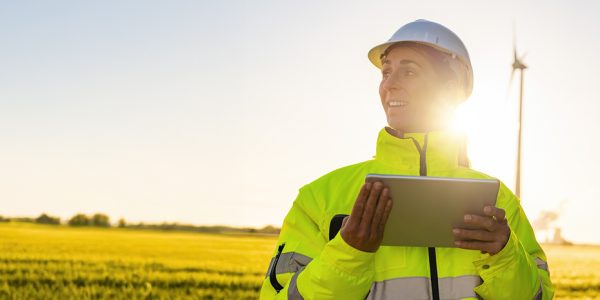 Young female engineer holding tablet looking and checking wind turbines at field