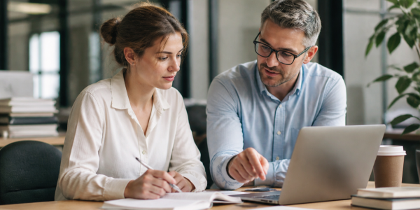 An experienced manager mentors a young professional during a one-on-one meeting, discussing work and career development in a modern office environment.